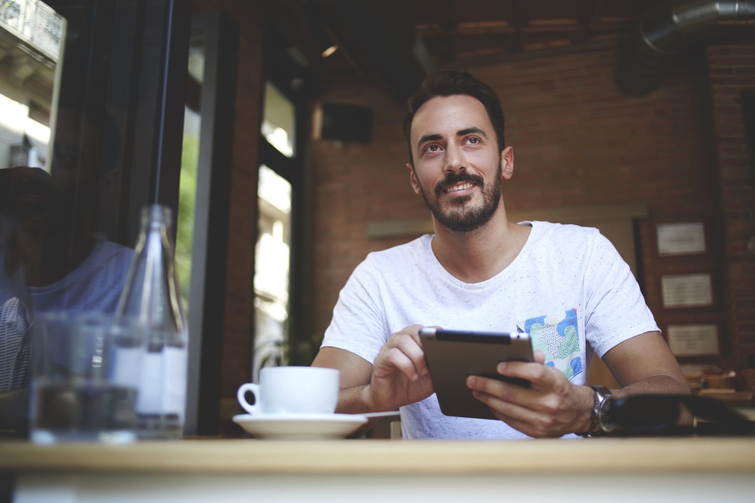 Male restaurateur with smile greets customers while working on digital tablet in own comfortable restaurant